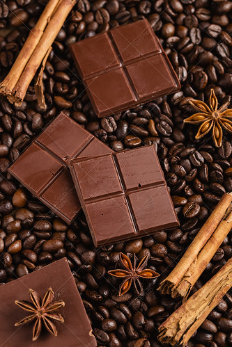 Chopped bitter chocolate with cinnamon sticks and anise stars on coffee beans background