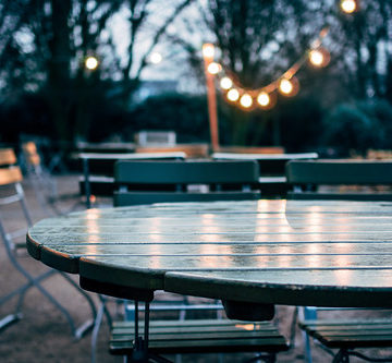 empty wooden chairs and tables in garden under electric light bulbs