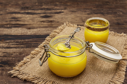 Pure or desi ghee (ghi), clarified melted butter. Healthy fats bulletproof diet concept or paleo style plan. Glass jar, silver spoon on vintage sackcloth. Wooden boards background