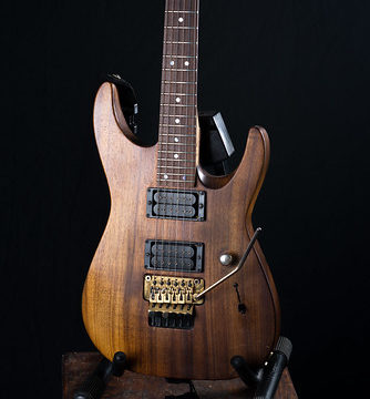 Charvel San Dimas koa on old wooden chair with a black background.