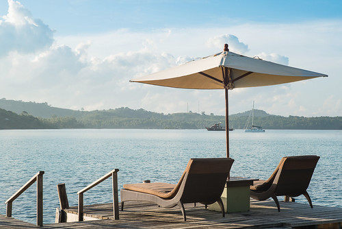 Two chairs and umbrella on wooden desk against blue sky